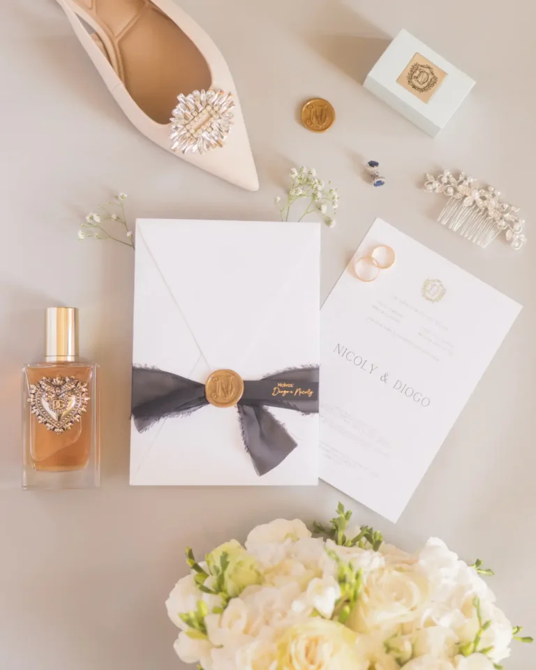 Fotografia flat-lay fine art de detalhes elegantes da noiva, incluindo convite de casamento em papel artesanal, alianças de ouro, sapatos de noiva de luxo e bouquet com flores orgânicas, captada com luz natural.