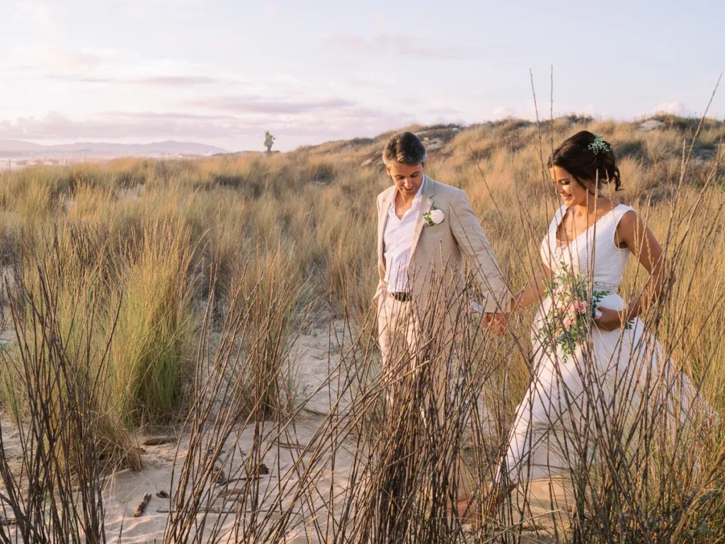 Fotografia fine art dos noivos a caminhar de forma orgânica na areia da praia durante a golden hour, banhados por uma luz quente natural.