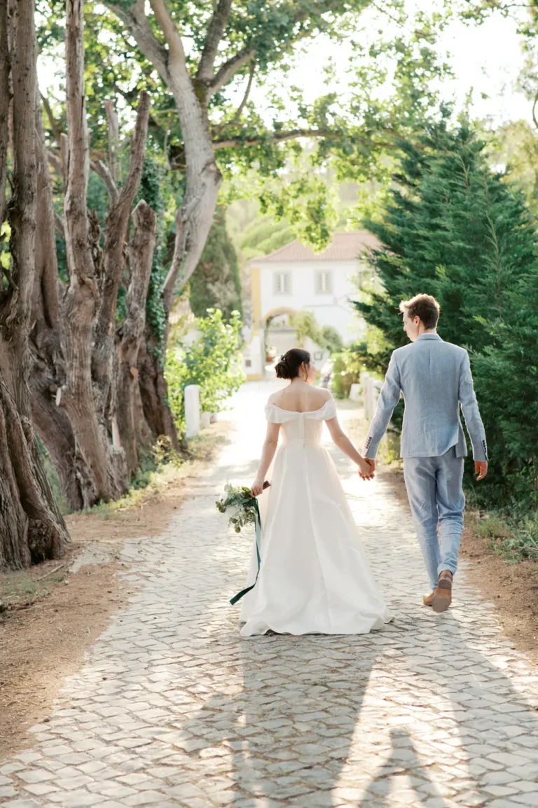 Fotografia fine art da Inês e do Ben a caminhar de forma descontraída na estrada empedrada da Quinta dos Machados, iluminados pela luz do pôr do sol pelas árvores.