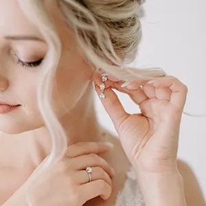 Close-up de uma noiva a colocar os seus brincos elegantes durante os preparativos, iluminada por luz natural suave.