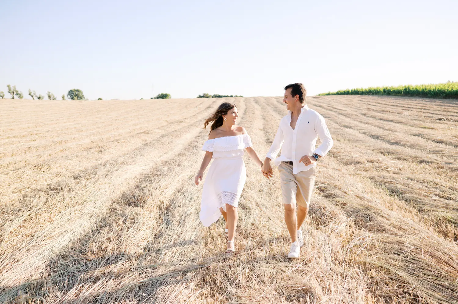 Luz de pôr do sol deslumbrante num campo de trigo recém-ceifado durante pre-wedding em Portugal.
