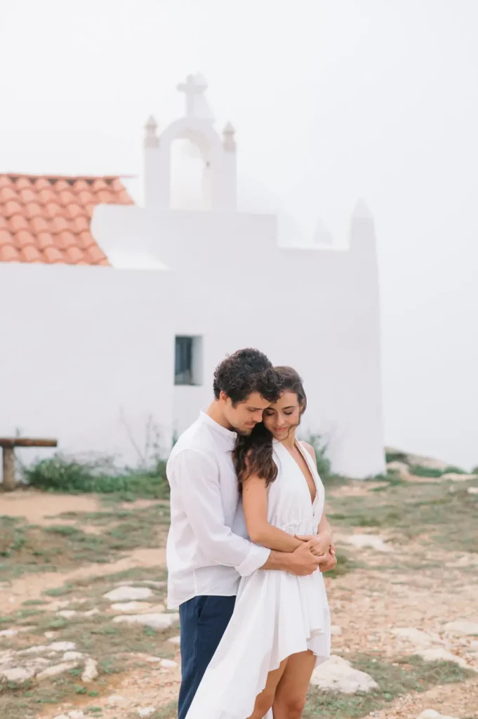 Casal de noivos brasileiros junto a capela branca no Baleal, sessão pre-wedding em Portugal.