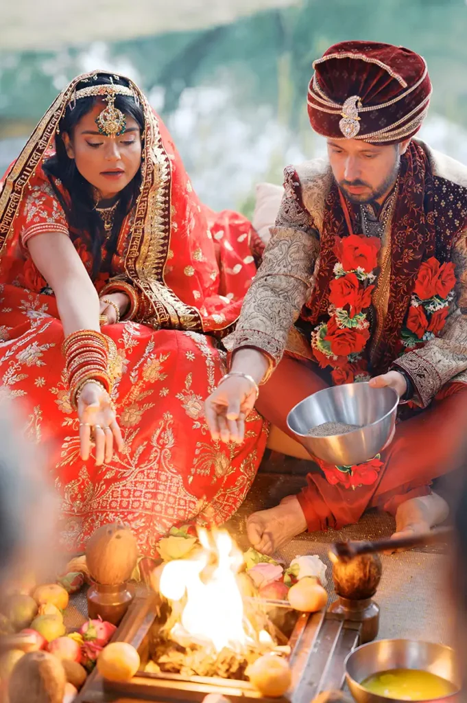 Casal feliz e sorridente durante os rituais sagrados da cerimónia de casamento hindu sob um exuberante Mandap floral num palácio em Sintra.