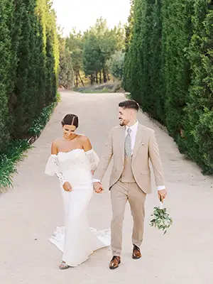 Newlyweds Joana and Diogo walk hand in hand on a trail lined by tall trees at Quinta do Valle do Riacho, showcasing a natural and elegant style.